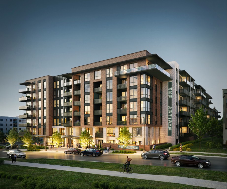 Modern mid-rise apartment building at dusk with lit windows, people outside, and a cyclist on the street in front.