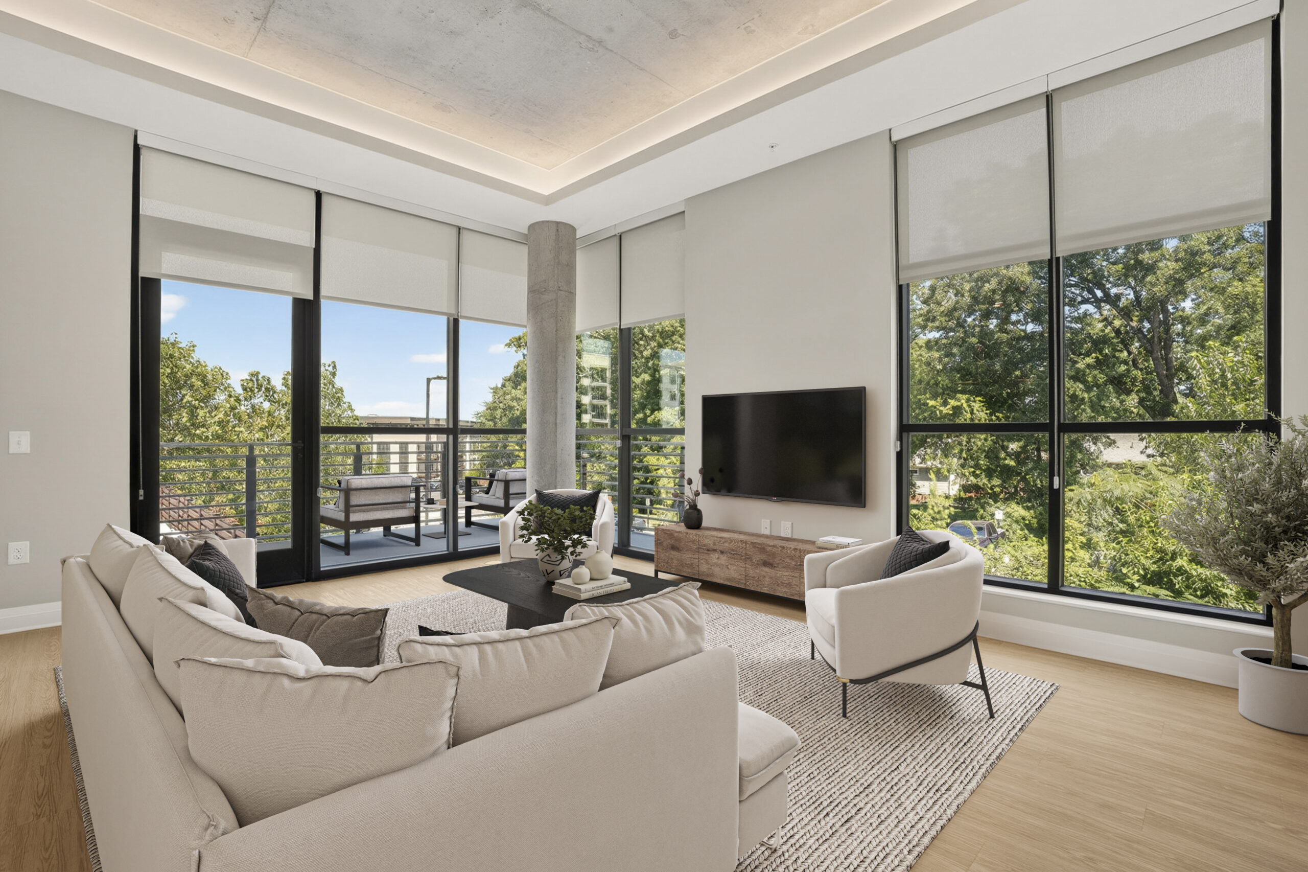 A modern living room with a sectional sofa, two armchairs, a coffee table, and a wall-mounted television, with large windows overlooking trees.