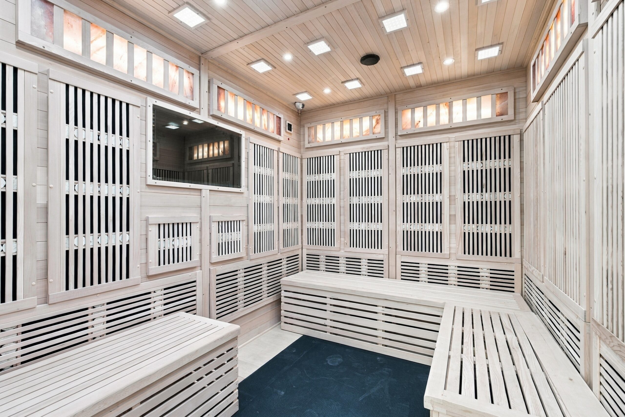 An empty sauna room with light wood paneling, benches, and illuminated salt brick accents.