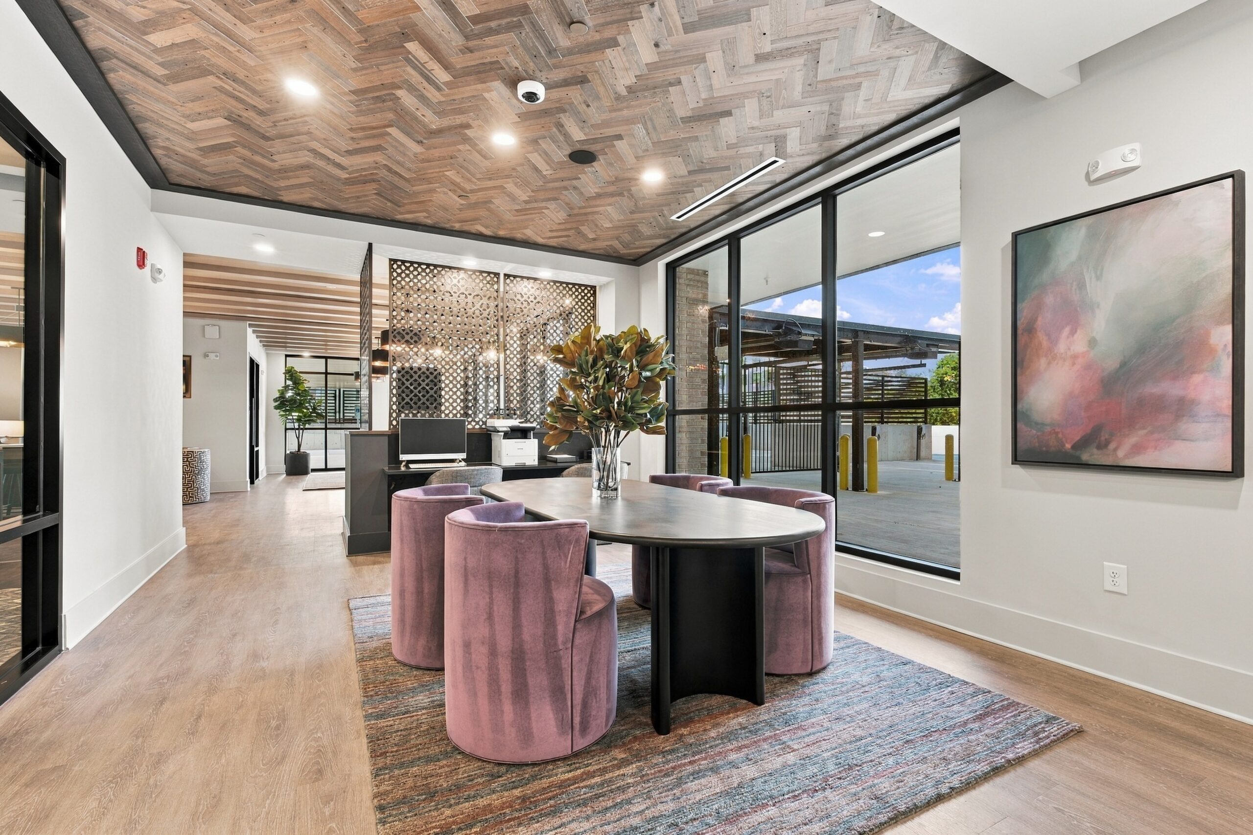 A small oval meeting table with four pink upholstered chairs in a modern office space.