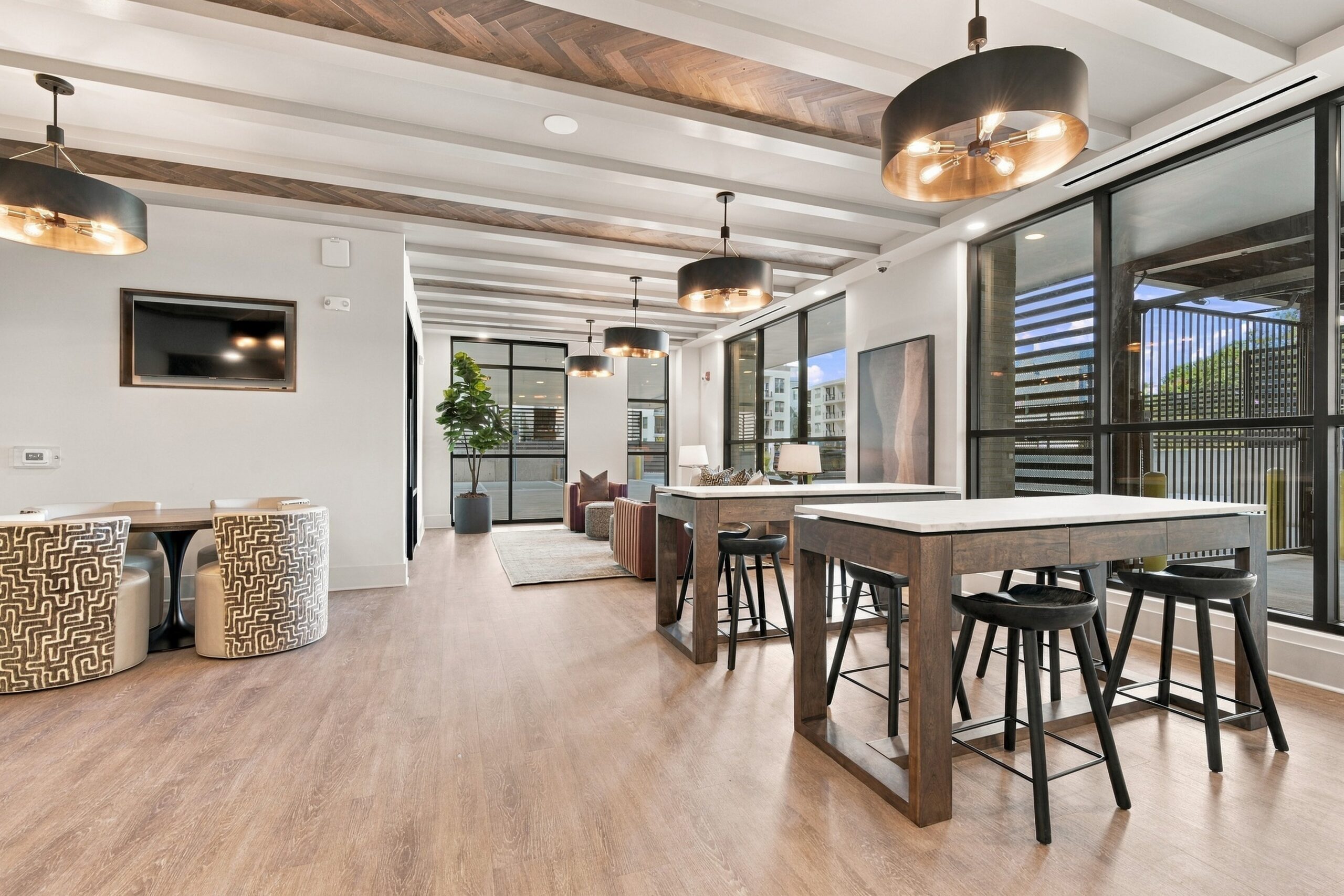A modern apartment lounge with high-top tables, bar stools, and a seating area with a television.