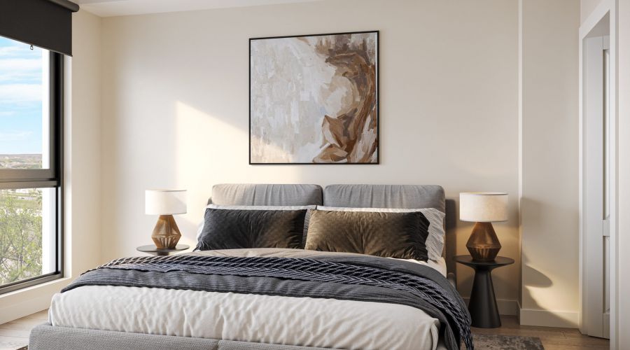 Modern bedroom with a gray bed, abstract wall art, two lamps on side tables, large window, and a neutral-colored rug.