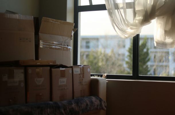 Moving boxes stacked near a window with sheer curtains blowing in sunlight.