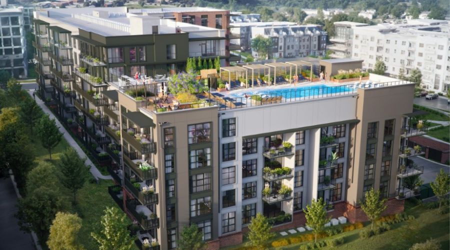 A modern apartment building with balconies, rooftop pool, and lounge area, surrounded by trees and other buildings.