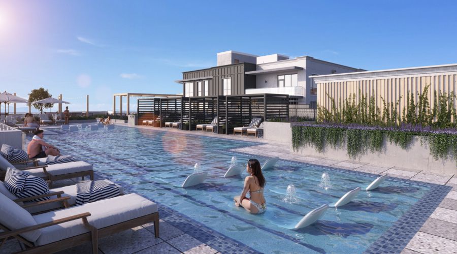People relax on lounge chairs and in a modern rooftop pool with fountains, under a clear blue sky.