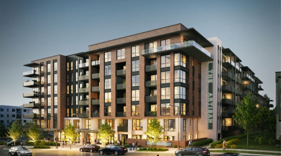 Modern mid-rise apartment building at dusk with lit windows, people outside, and a cyclist on the street in front.